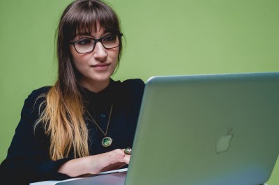 Young person with glasses uses a Macbook against a green background