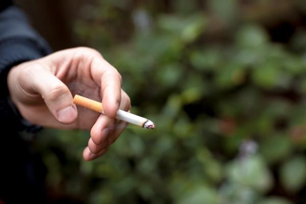 Shot of a single hand holding a lit, half-smoked cigarette between two fingers